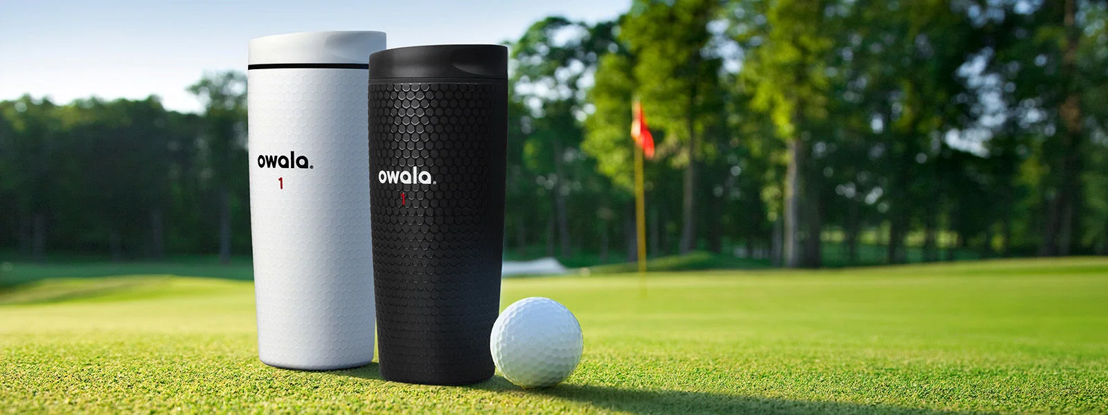 Two owala bottles and a golf ball on a golf course.