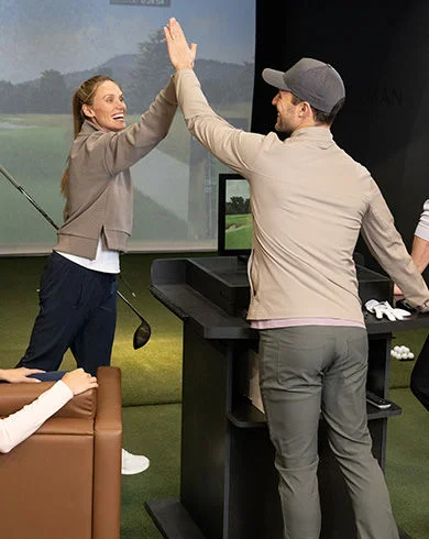 People high-fiving at a golf simulator.