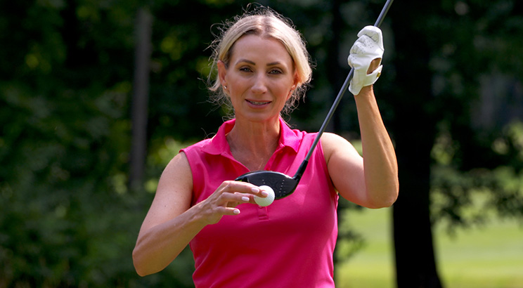 An image of a golfer holding up a golf ball and club. 